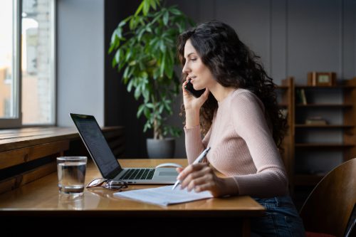 young-woman-talking-on-the-phone-while-working-on-the-computer-and-writing-notes