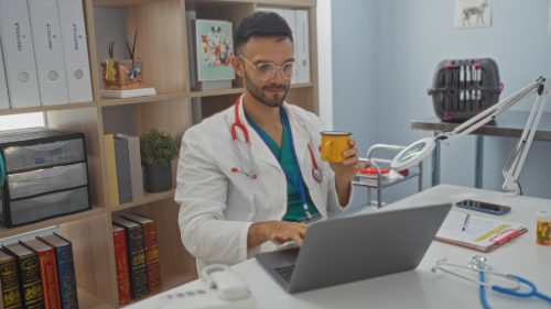 male-vet-working-in-a-clinic-office-on-a-laptop-while-drinking-coffee